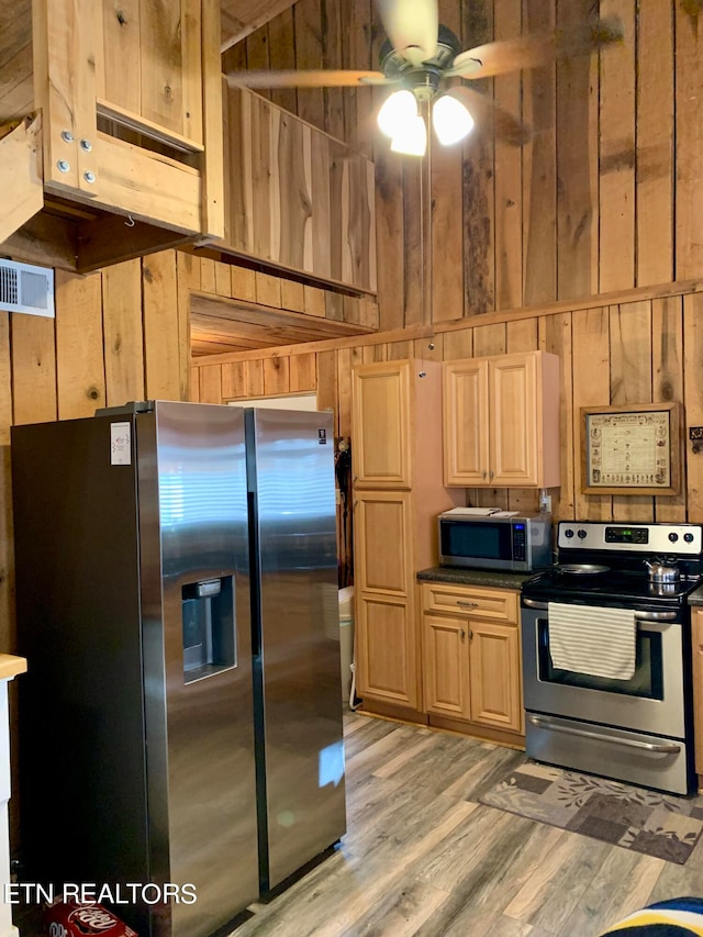 kitchen with light hardwood / wood-style floors, wood walls, and appliances with stainless steel finishes