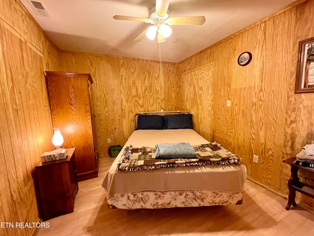 bedroom featuring ceiling fan, light hardwood / wood-style flooring, and wood walls