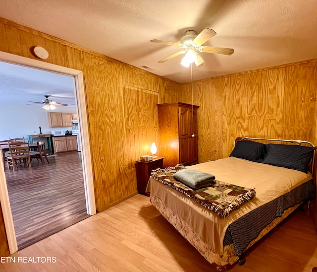 bedroom featuring hardwood / wood-style flooring, ceiling fan, and wood walls