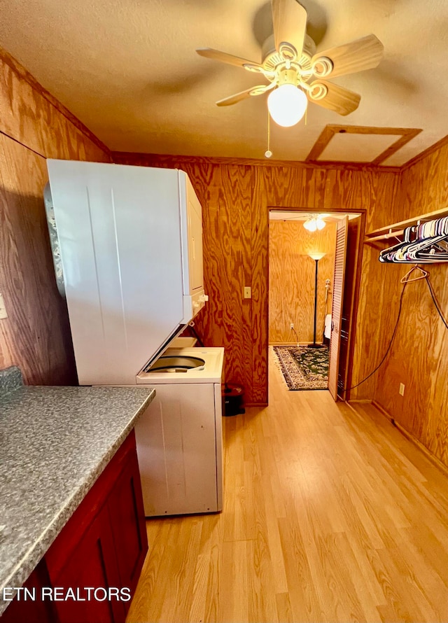 kitchen featuring stacked washing maching and dryer, wooden walls, ceiling fan, and light wood-type flooring