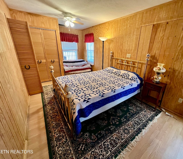 bedroom with a textured ceiling, hardwood / wood-style flooring, wooden walls, a closet, and ceiling fan