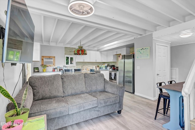 living room featuring an AC wall unit, beamed ceiling, sink, and light hardwood / wood-style floors