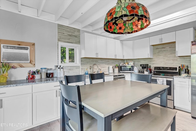 kitchen with light hardwood / wood-style floors, an AC wall unit, backsplash, white cabinets, and appliances with stainless steel finishes