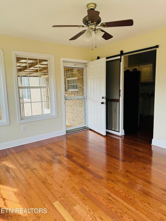 spare room with ceiling fan, a barn door, and hardwood / wood-style flooring