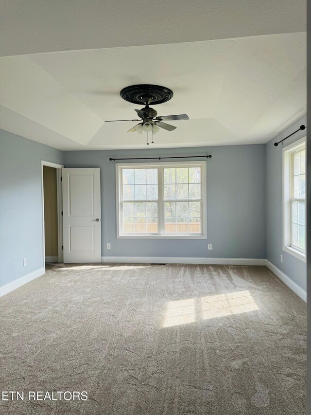 empty room featuring ceiling fan, plenty of natural light, light colored carpet, and a raised ceiling