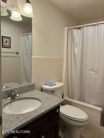 full bathroom with toilet, vanity, tile walls, and shower / tub combo with curtain