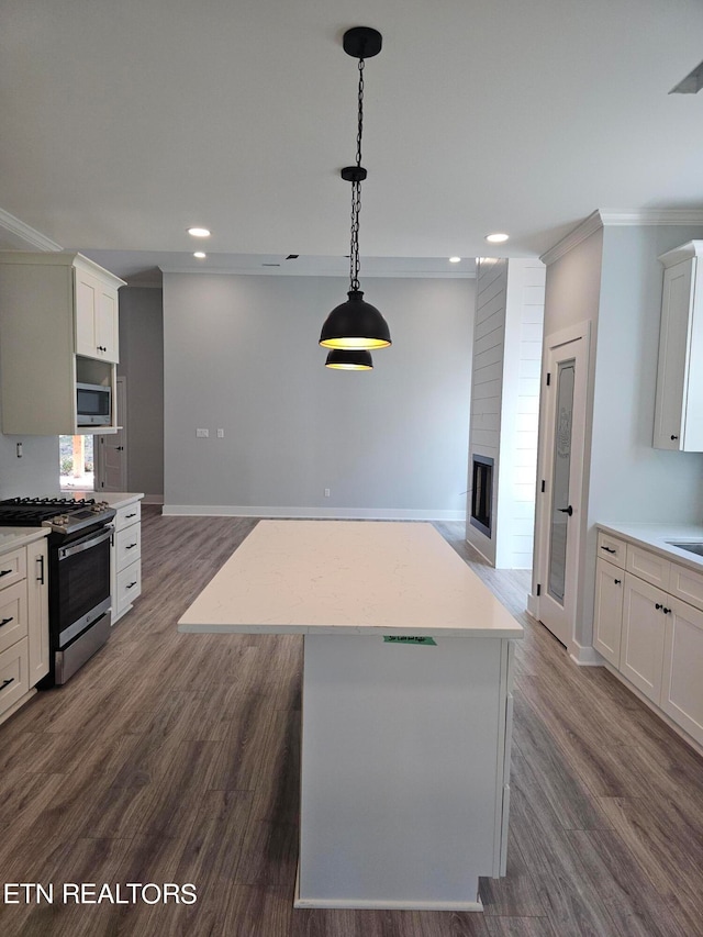 kitchen with dark wood-type flooring, a fireplace, white cabinets, appliances with stainless steel finishes, and a center island