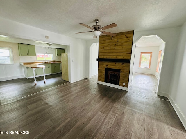 unfurnished living room with a healthy amount of sunlight, dark wood-type flooring, and wooden walls