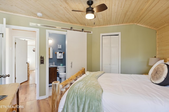 bedroom featuring wood ceiling, a barn door, ceiling fan, ensuite bath, and a closet