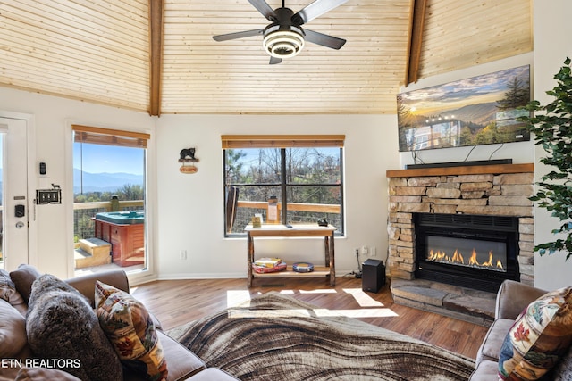 living room with ceiling fan, wood ceiling, a stone fireplace, and lofted ceiling with beams