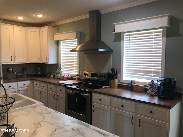 kitchen featuring wall chimney range hood, backsplash, crown molding, white cabinetry, and electric stove