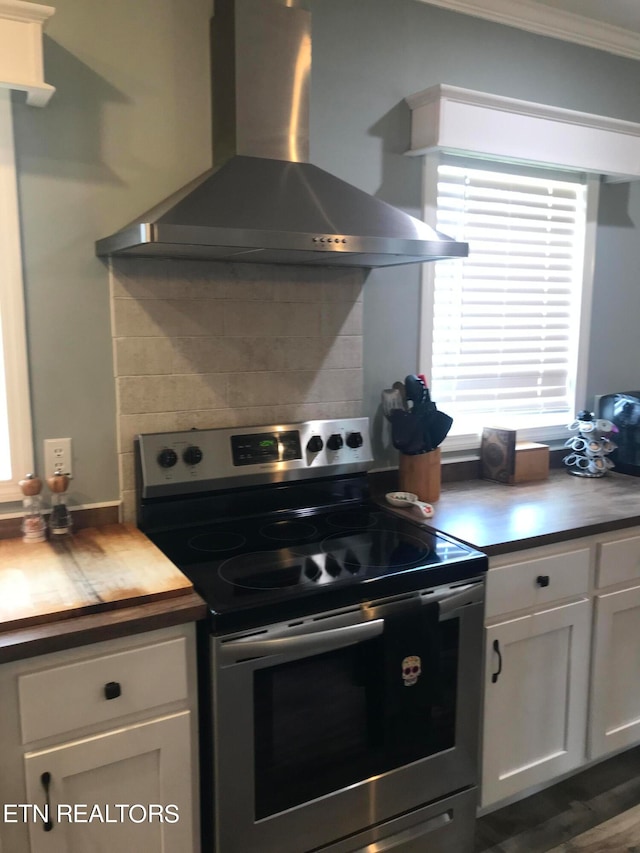 kitchen with crown molding, stainless steel electric range, backsplash, wall chimney exhaust hood, and white cabinets