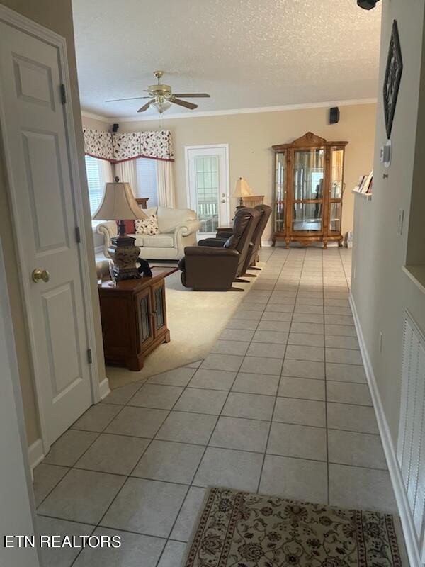 tiled living room with a textured ceiling, ornamental molding, and ceiling fan