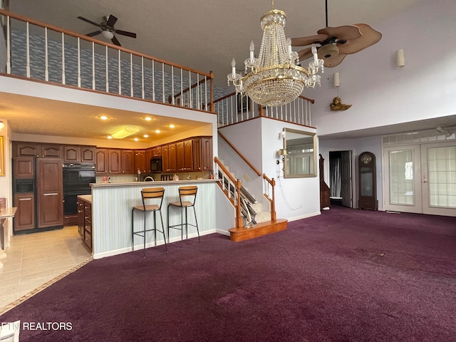 unfurnished living room featuring a towering ceiling, light carpet, and ceiling fan with notable chandelier