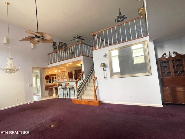 unfurnished living room with a high ceiling, ceiling fan with notable chandelier, and carpet flooring