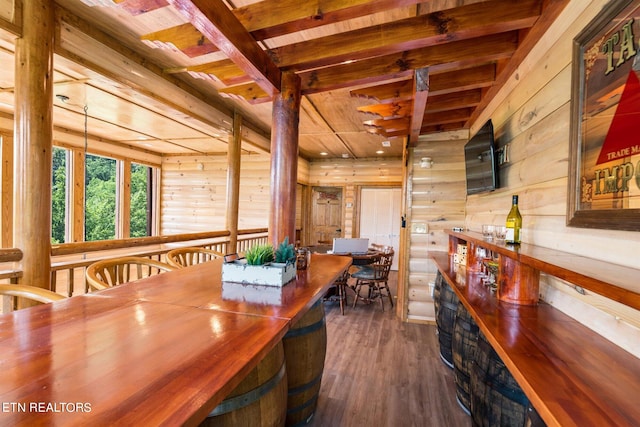 dining room with dark wood-type flooring, wooden walls, beamed ceiling, and indoor bar