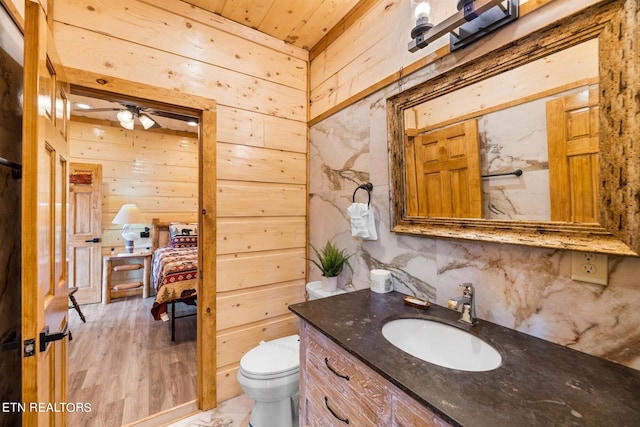 bathroom featuring ceiling fan, hardwood / wood-style flooring, wooden walls, vanity, and toilet