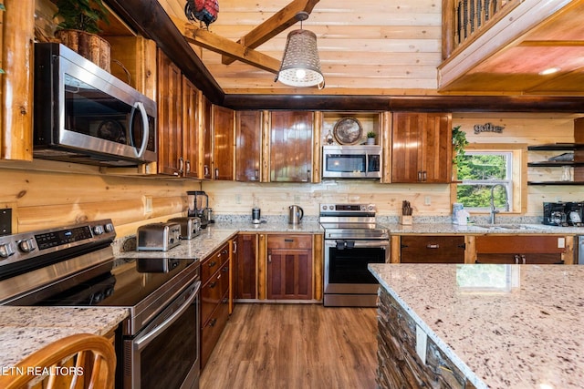 kitchen featuring light stone countertops, stainless steel appliances, decorative light fixtures, sink, and hardwood / wood-style flooring