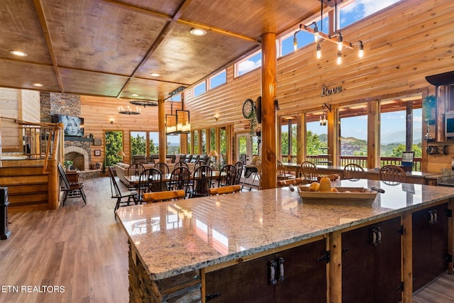 kitchen featuring light stone counters, wooden ceiling, a stone fireplace, wood-type flooring, and wooden walls