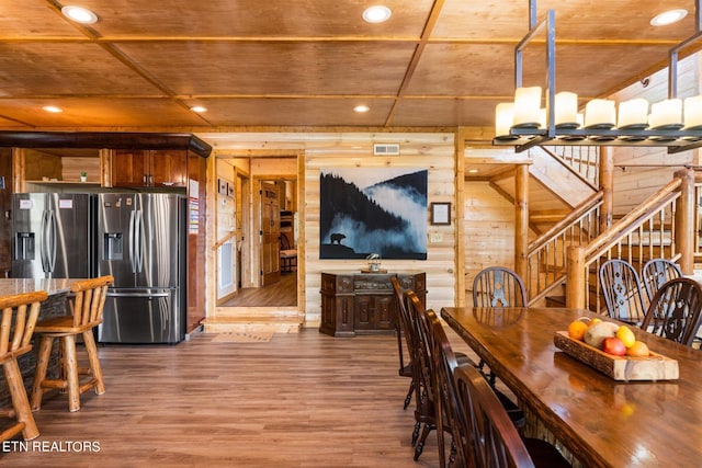 dining room featuring wood-type flooring, wooden walls, and an inviting chandelier