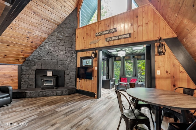 dining space featuring wood ceiling, wood-type flooring, a wood stove, wooden walls, and high vaulted ceiling