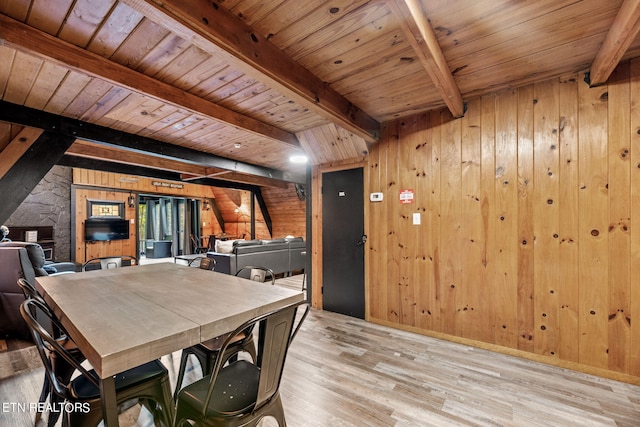 unfurnished dining area with beamed ceiling, wood walls, light wood-type flooring, and wooden ceiling