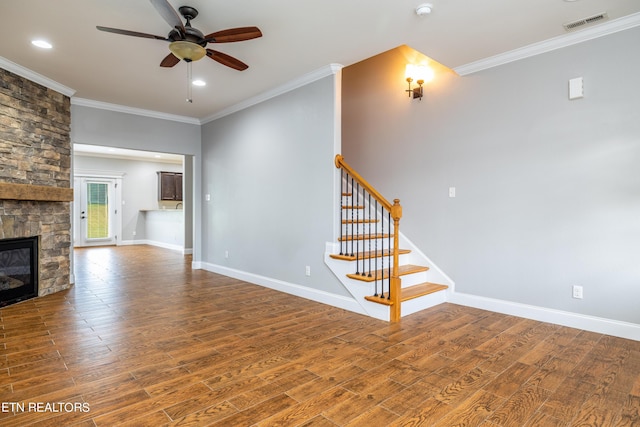 unfurnished living room with ceiling fan, crown molding, wood-type flooring, and a stone fireplace