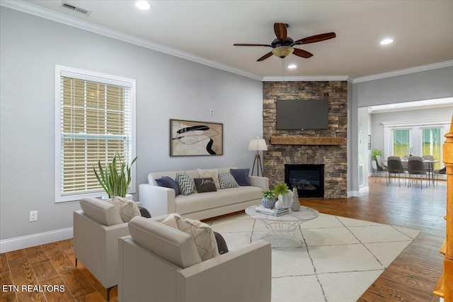 living room featuring ceiling fan, a stone fireplace, ornamental molding, and hardwood / wood-style flooring