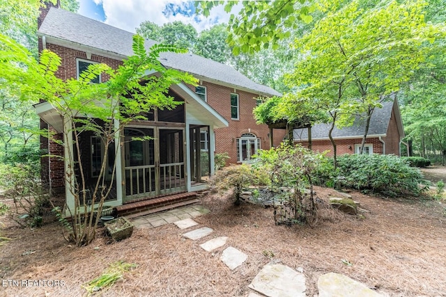 rear view of house with brick siding, a sunroom, and a shingled roof
