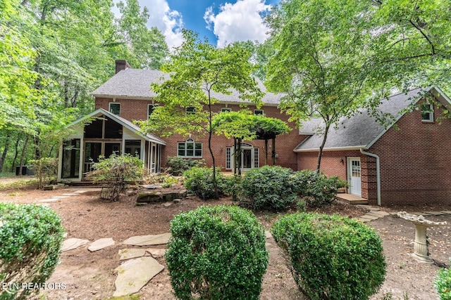 rear view of house with brick siding, a sunroom, and a chimney