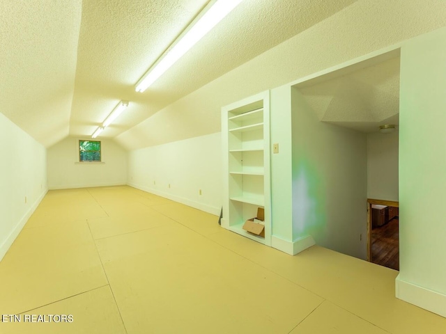 bonus room with built in features, lofted ceiling, a textured ceiling, and baseboards