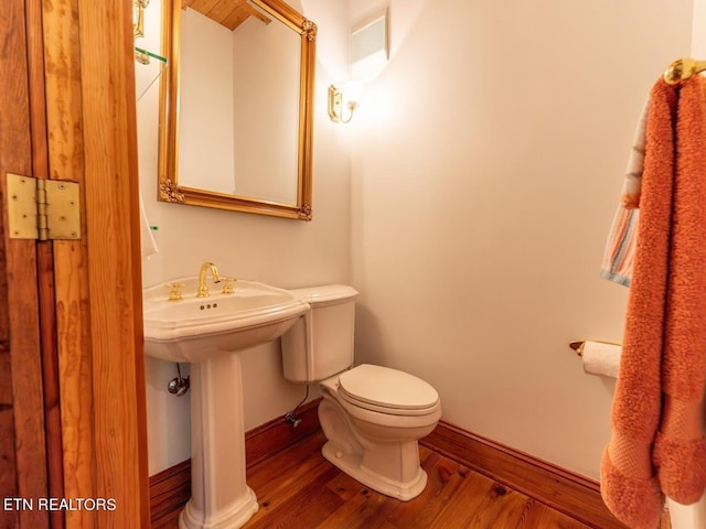 half bathroom featuring toilet, wood finished floors, and baseboards