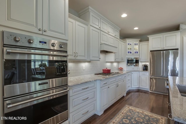 kitchen with light stone countertops, appliances with stainless steel finishes, white cabinetry, and dark wood-type flooring