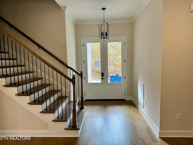 foyer entrance featuring dark wood-type flooring, a chandelier, french doors, and ornamental molding