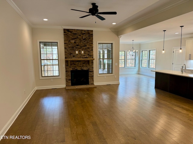 unfurnished living room featuring a stone fireplace, sink, dark wood-type flooring, and ceiling fan with notable chandelier