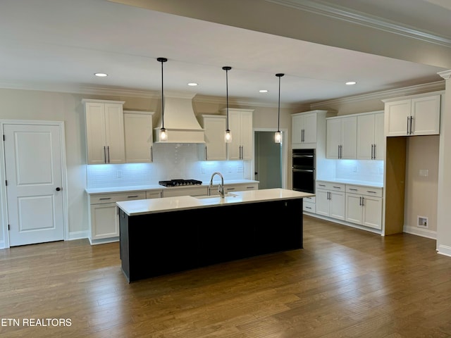 kitchen with white cabinetry, hanging light fixtures, gas stovetop, a kitchen island with sink, and custom range hood