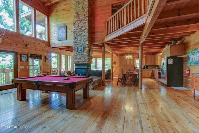 game room with a stone fireplace, billiards, light wood-type flooring, a towering ceiling, and beamed ceiling