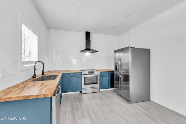 kitchen featuring appliances with stainless steel finishes, wall chimney exhaust hood, wood counters, and sink