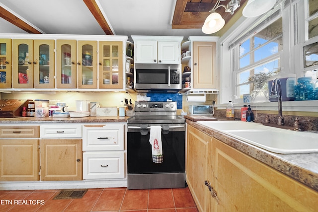 kitchen with stainless steel appliances, sink, light brown cabinets, beamed ceiling, and tile patterned flooring