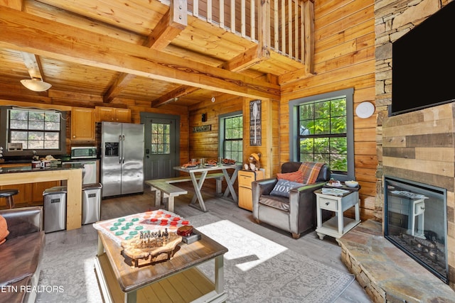 living room with wood-type flooring, wooden walls, a stone fireplace, and a healthy amount of sunlight