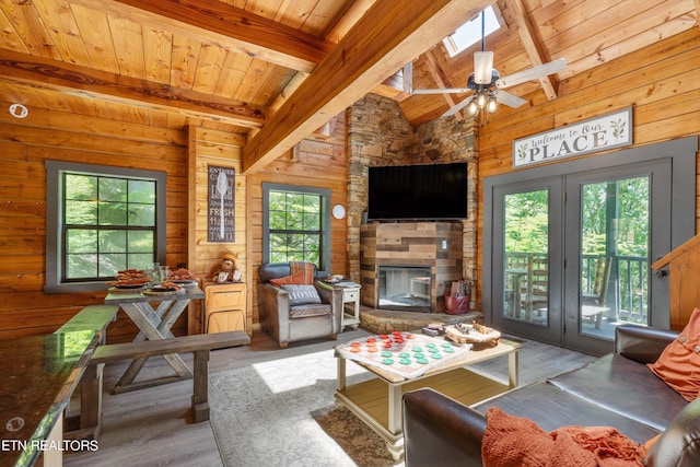 living room with ceiling fan, wood walls, beamed ceiling, a skylight, and wooden ceiling