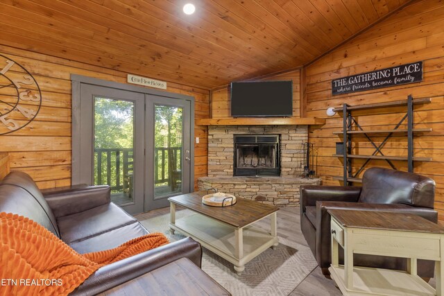 living room with light hardwood / wood-style floors, a stone fireplace, wood ceiling, and vaulted ceiling