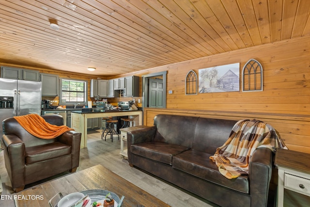 living room featuring light hardwood / wood-style floors, sink, wood walls, and wood ceiling