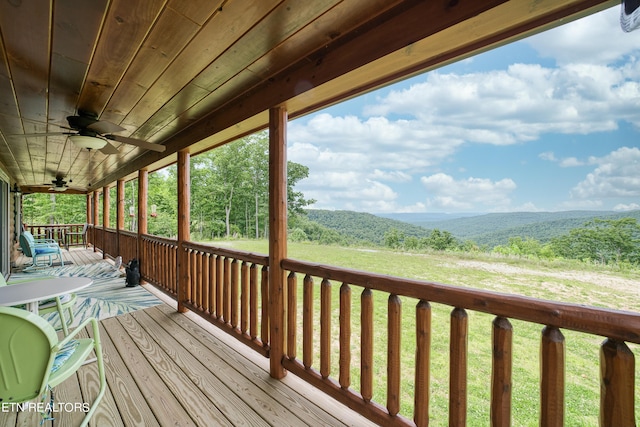 wooden deck featuring ceiling fan, a yard, and a mountain view