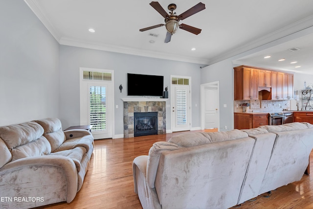 living room with ceiling fan, ornamental molding, a fireplace, and light hardwood / wood-style flooring