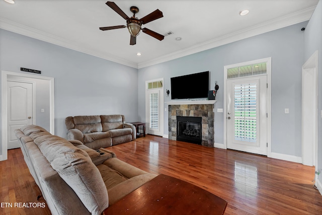 living room with ceiling fan, crown molding, hardwood / wood-style flooring, and a stone fireplace