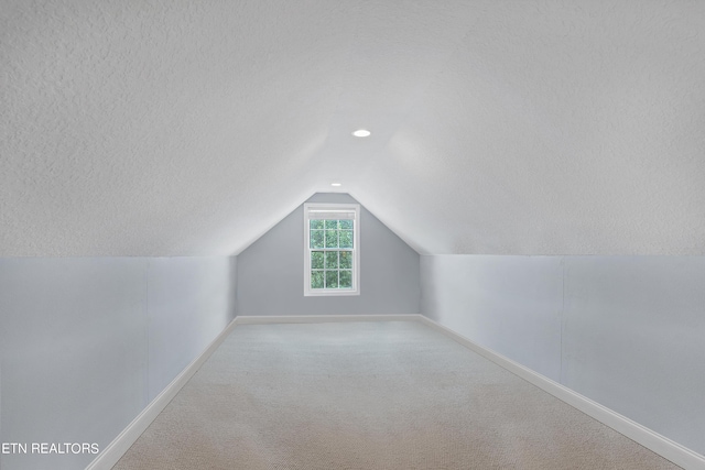 additional living space featuring vaulted ceiling, a textured ceiling, and light carpet