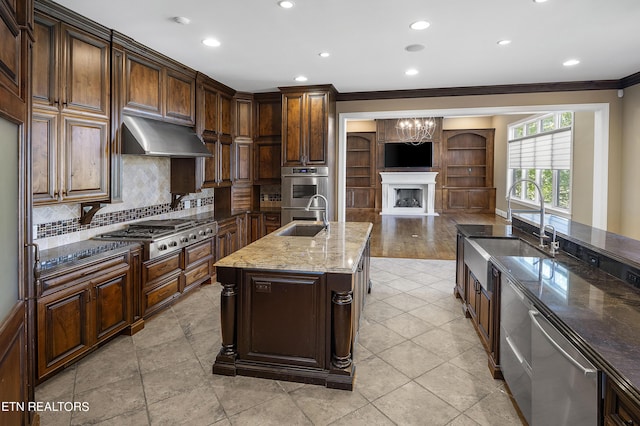 kitchen with sink, dark stone countertops, tasteful backsplash, a kitchen island with sink, and appliances with stainless steel finishes