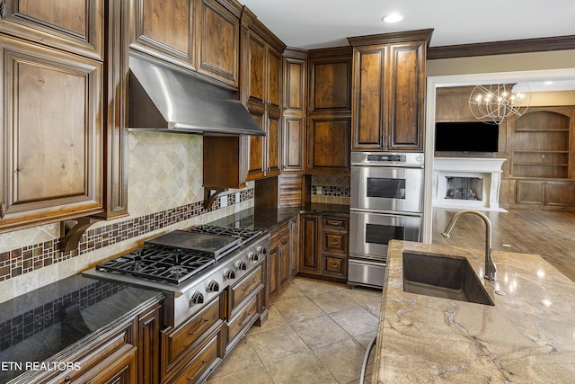 kitchen with a notable chandelier, tasteful backsplash, dark stone counters, appliances with stainless steel finishes, and sink