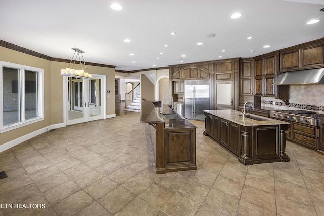 kitchen featuring appliances with stainless steel finishes, hanging light fixtures, an island with sink, sink, and dark brown cabinets